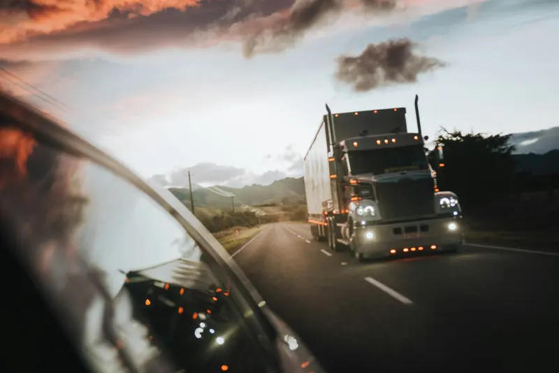 Carreta na rodovia vista pelo retrovisor, ao entardecer